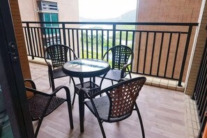 A balcony with a round table and four chairs, a view of greenery, and a brick wall. - Youzhan Hostel (Shenzhen)