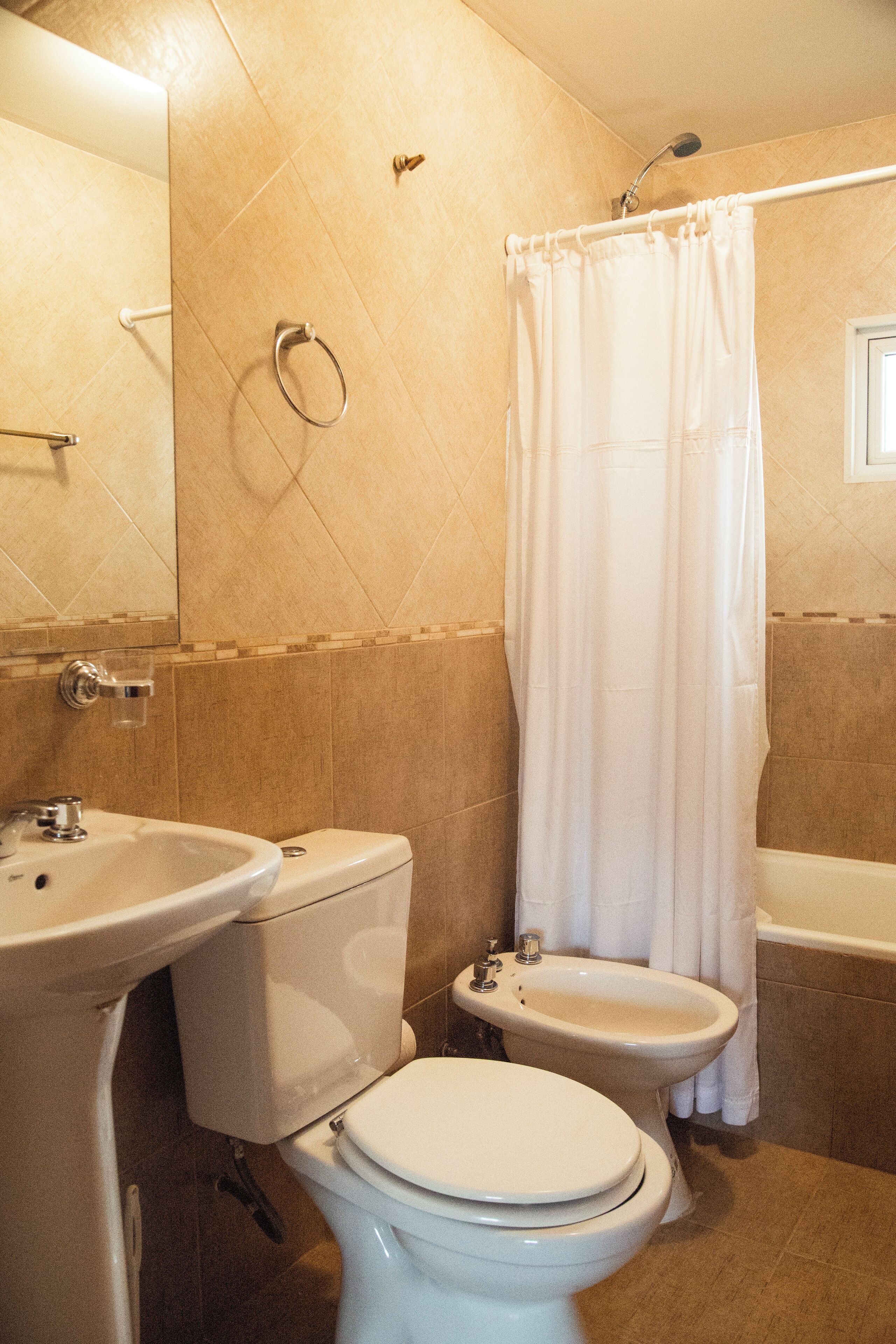 A bathroom with a toilet, bidet, sink, and shower curtain.