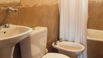 A bathroom with a toilet, bidet, sink, and shower curtain.