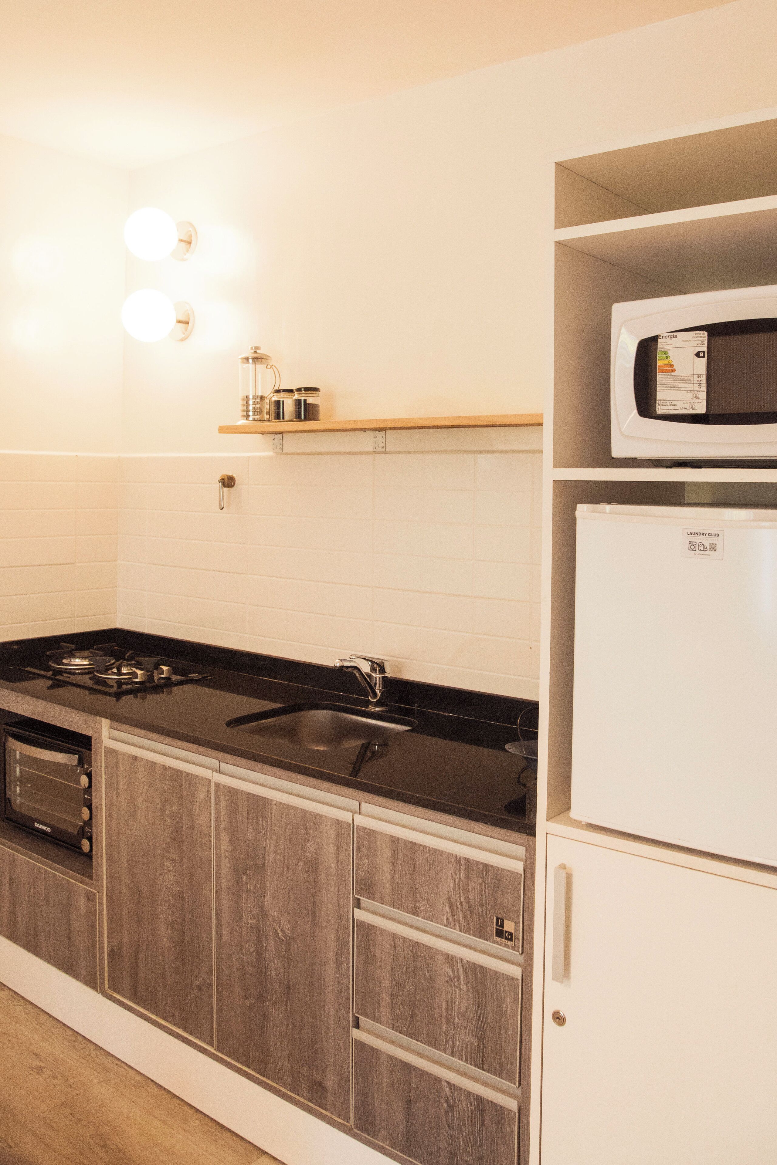 A kitchen with a black countertop, white cabinets, a microwave, and a refrigerator.