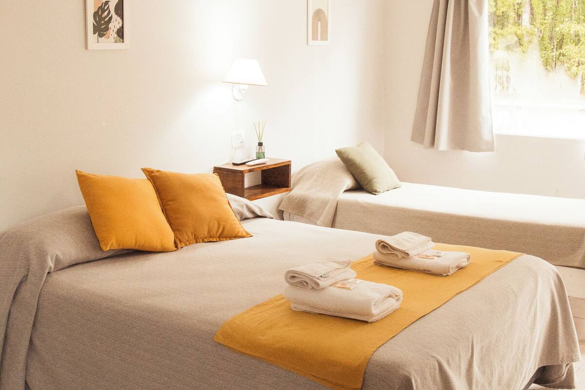 Un dormitorio con dos camas, una mesita de noche, una lámpara y una ventana con cortinas.