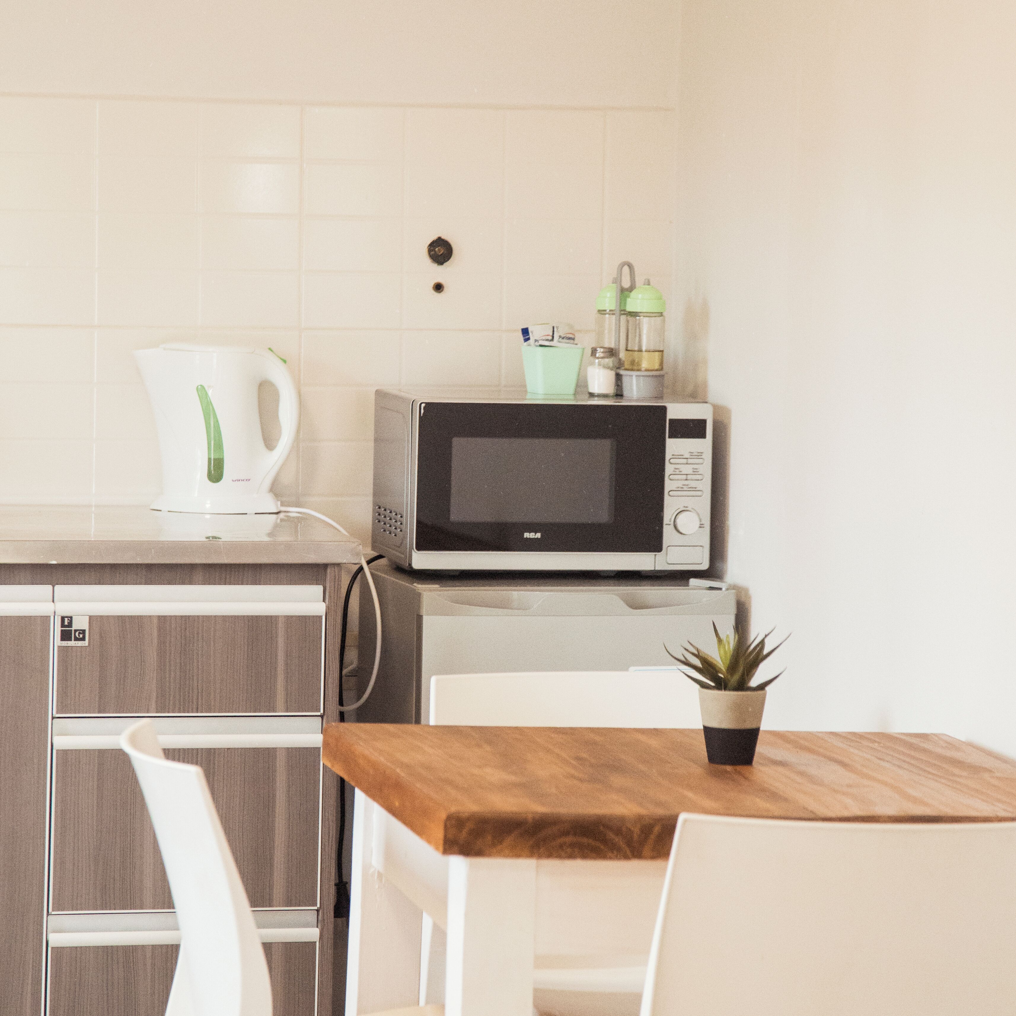 Una cocina con microondas, cafetera y una pequeña planta en maceta sobre la mesa.