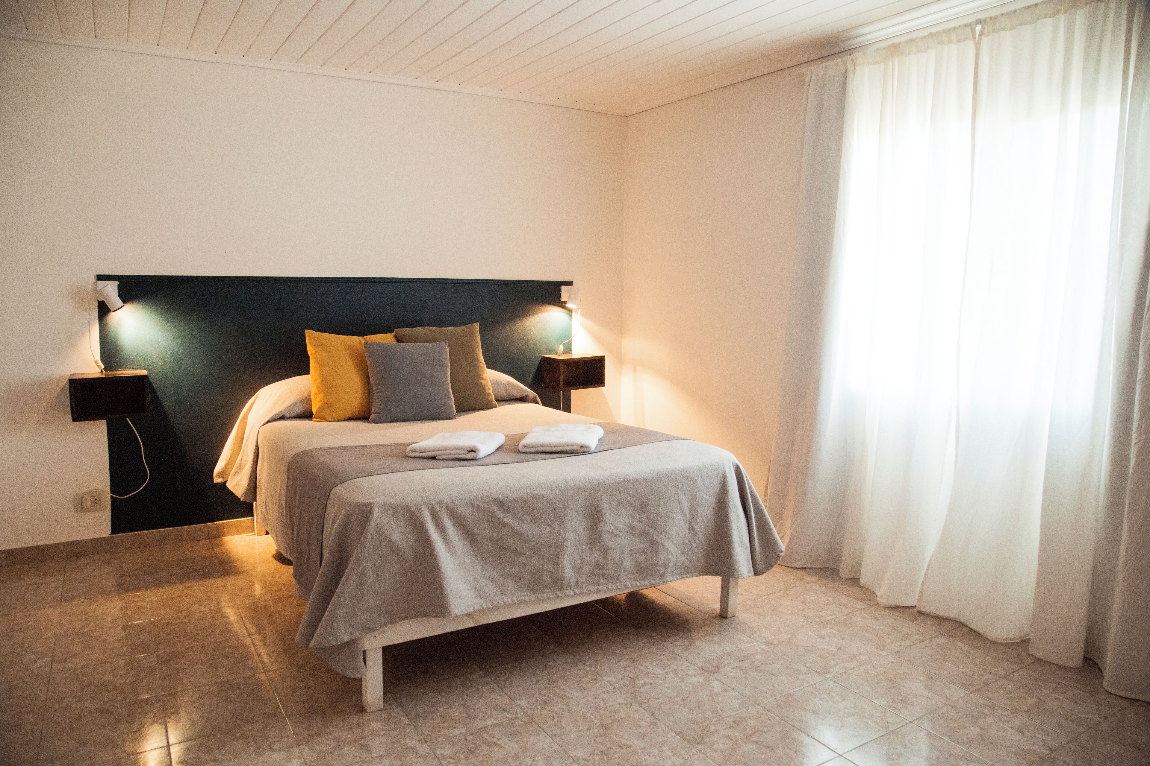 A bedroom with a bed, bedside lamps, and a window with curtains.