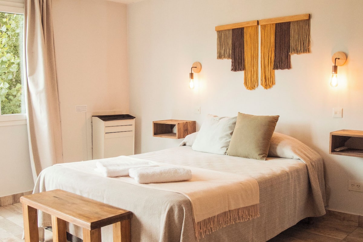 Un dormitorio con una cama grande, mesitas de noche, un banco de madera y un escritorio.