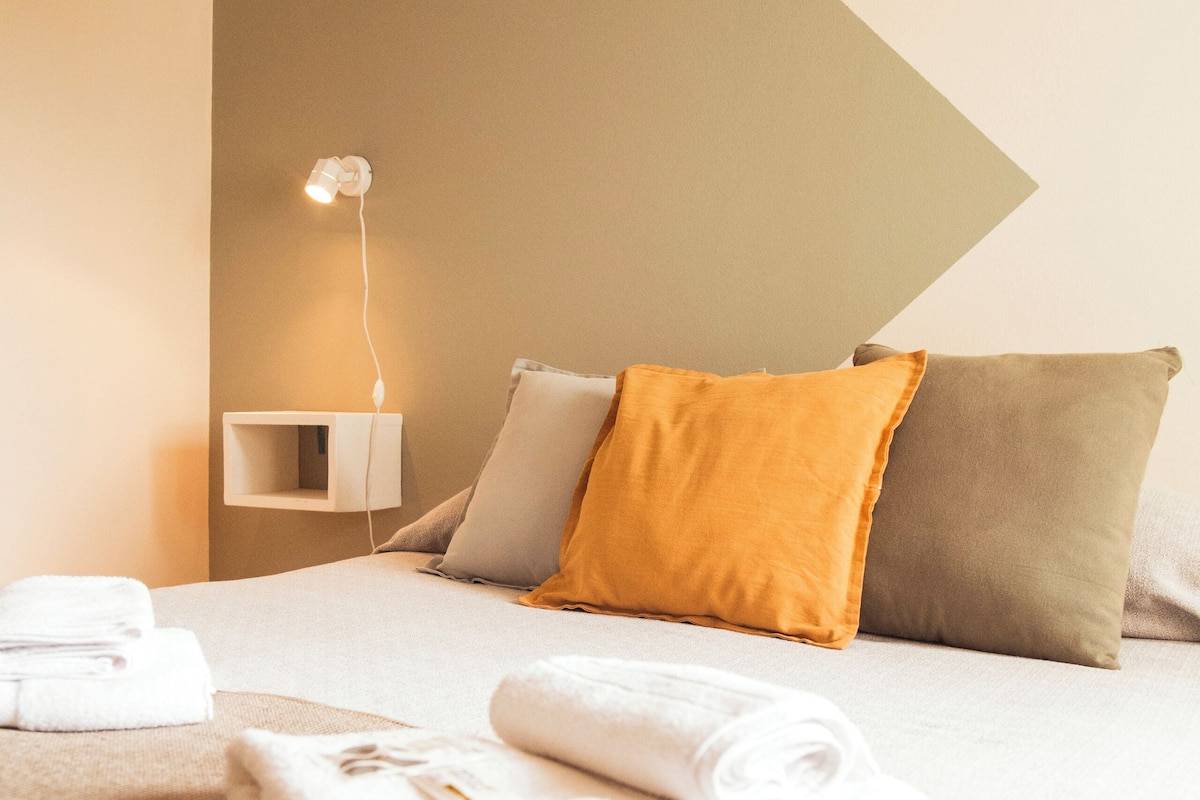 Una cama bien hecha con toallas dobladas, una lámpara de noche y dos almohadas en una habitación moderna con techo inclinado.