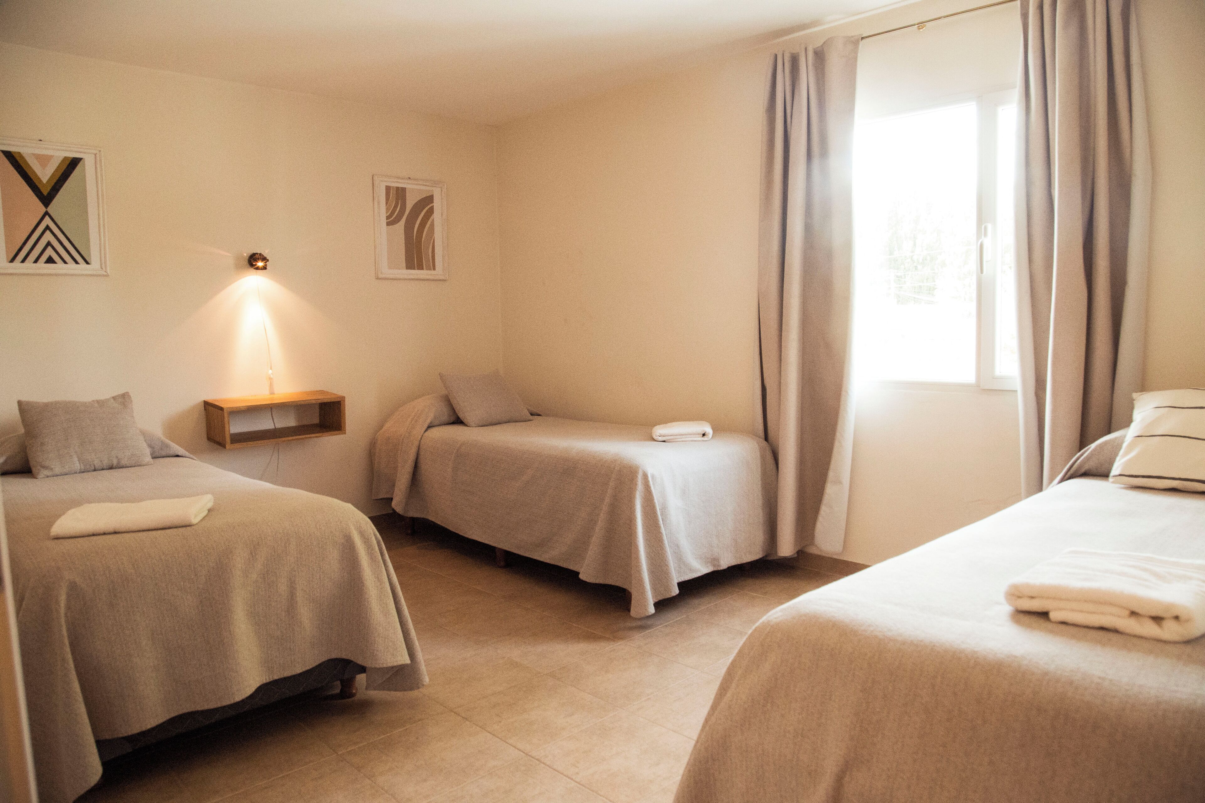 A hotel room with two single beds, a bedside table with a lamp, and a window with curtains.