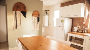 Eine Küche mit einem Holztisch, weißen Stühlen, einem weißen Kühlschrank und einem Durchlauferhitzer.