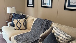 Un salon avec un canapé beige, une lampe et des cartes encadrées accrochées au mur.