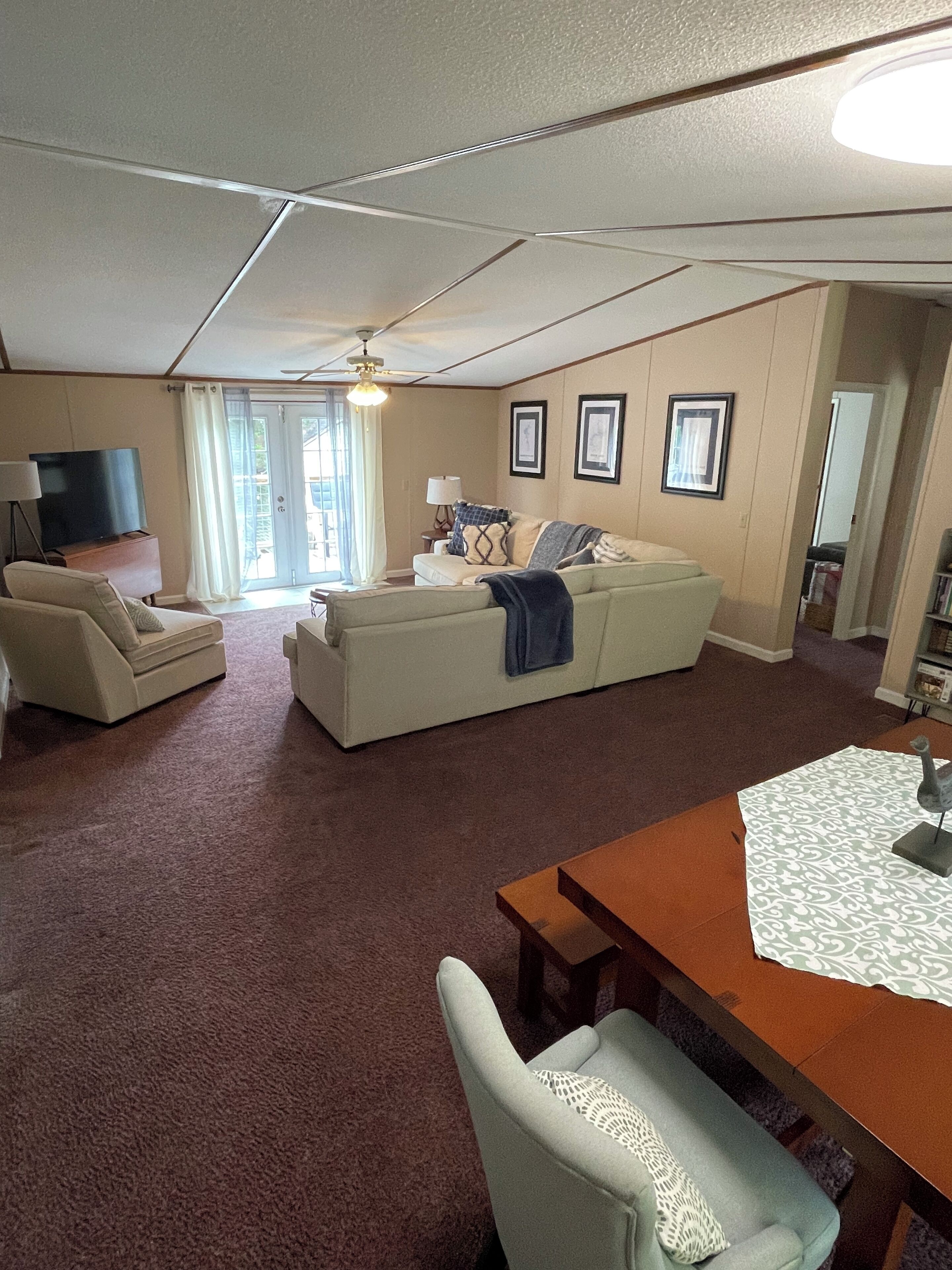 A spacious living room with a large sofa, a dining table with a placemat, and a television.