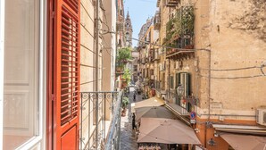 A narrow street with buildings on either side, outdoor seating with umbrellas, and a visible sign for a restaurant. - Il Cortile degli Aragonesi by Wonderful Italy (Palermo)