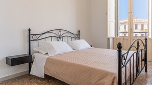 Een slaapkamer met een bed, een nachtkastje en een raam met uitzicht op gebouwen.