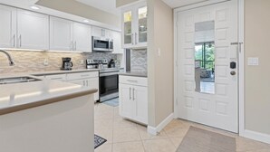 Een moderne keuken met witte kasten, een roestvrijstalen spoelbak, een magnetron en een fornuis. Er is een glazen deur die leidt naar een balkon.
