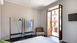Ein Schlafzimmer mit einem Bett, einem Kleiderschrank, einem Sessel und einer Glastür zum Balkon.