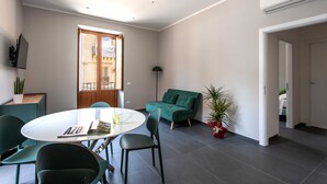Ein modernes Wohnzimmer mit einem runden Tisch, grünen Sesseln, einem grünen Sofa und einer Topfpflanze.