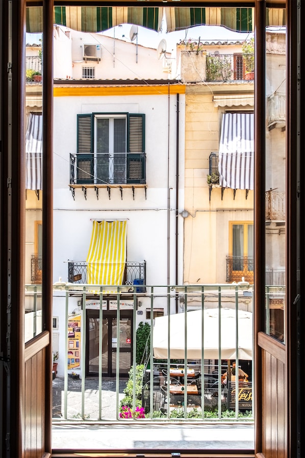 A view from a balcony overlooking a street with buildings, a yellow-striped awning, and a metal railing.
