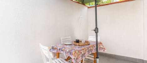 A patio area with a table and chairs under a green umbrella, a tiled floor, and a white wall.
