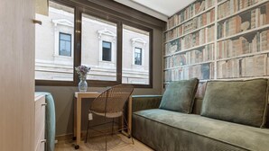 A cozy room with a green sofa, a wicker chair, a small table with a vase, and a bookshelf with books.