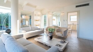Amplia sala de estar con sofá, sillones y una mesa de centro. Se ve una cocina y un comedor a través de un umbral abierto.