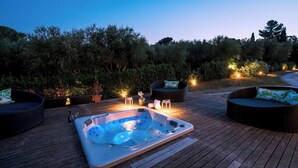 Un jacuzzi en una terraza de madera con mobiliario exterior e iluminación ambiental.