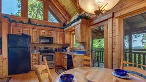 A wooden cabin kitchen with a dining table, chairs, and a view of the outdoors. - Relaxing 3BD Cabin w/ HOT TUB! Pool Table + GAMES! (Sevierville)