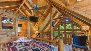 A log cabin bedroom with a bed, a chair, a ceiling fan, and a window. - Relaxing 3BD Cabin w/ HOT TUB! Pool Table + GAMES! (Sevierville)