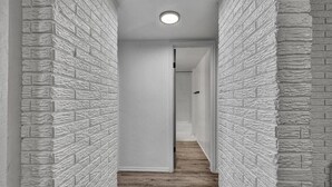Un pasillo estrecho con paredes blancas texturizadas y suelo de madera que conduce a una puerta al final.