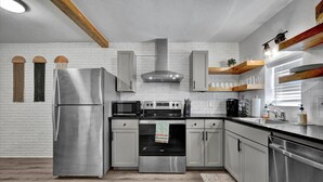 Una cocina moderna con electrodomésticos de acero inoxidable, vigas de madera y paredes de ladrillo blanco.