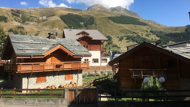 A mountain village with wooden houses, stone walls, and a clear view of the surrounding hills.