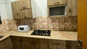 A kitchen with wooden cabinets, a microwave, and a gas stove. - Harvey's Apartment (Islamabad)