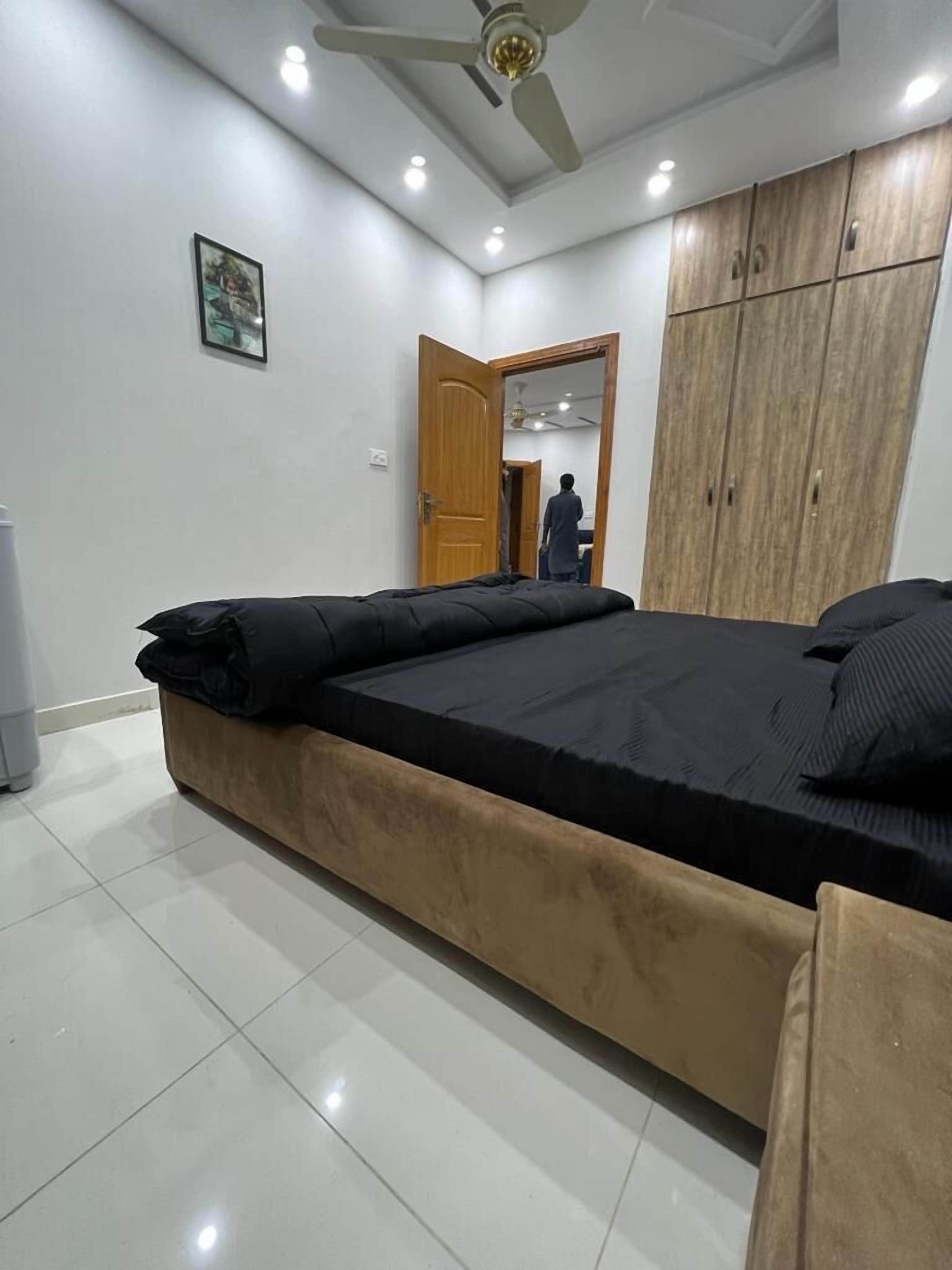 A bedroom with a bed, a wardrobe, a ceiling fan, and a door leading to another room.