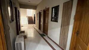 A corridor with tiled flooring, wooden doors, and a staircase in the background. - Harvey's Apartment (Islamabad)