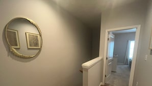 Un couloir avec un plancher en bois, une plinthe blanche et un miroir accroché au mur.
