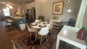 Une cuisine moderne avec un îlot central, des chaises blanches, une table à manger avec des sets de table et un tapis à motifs.