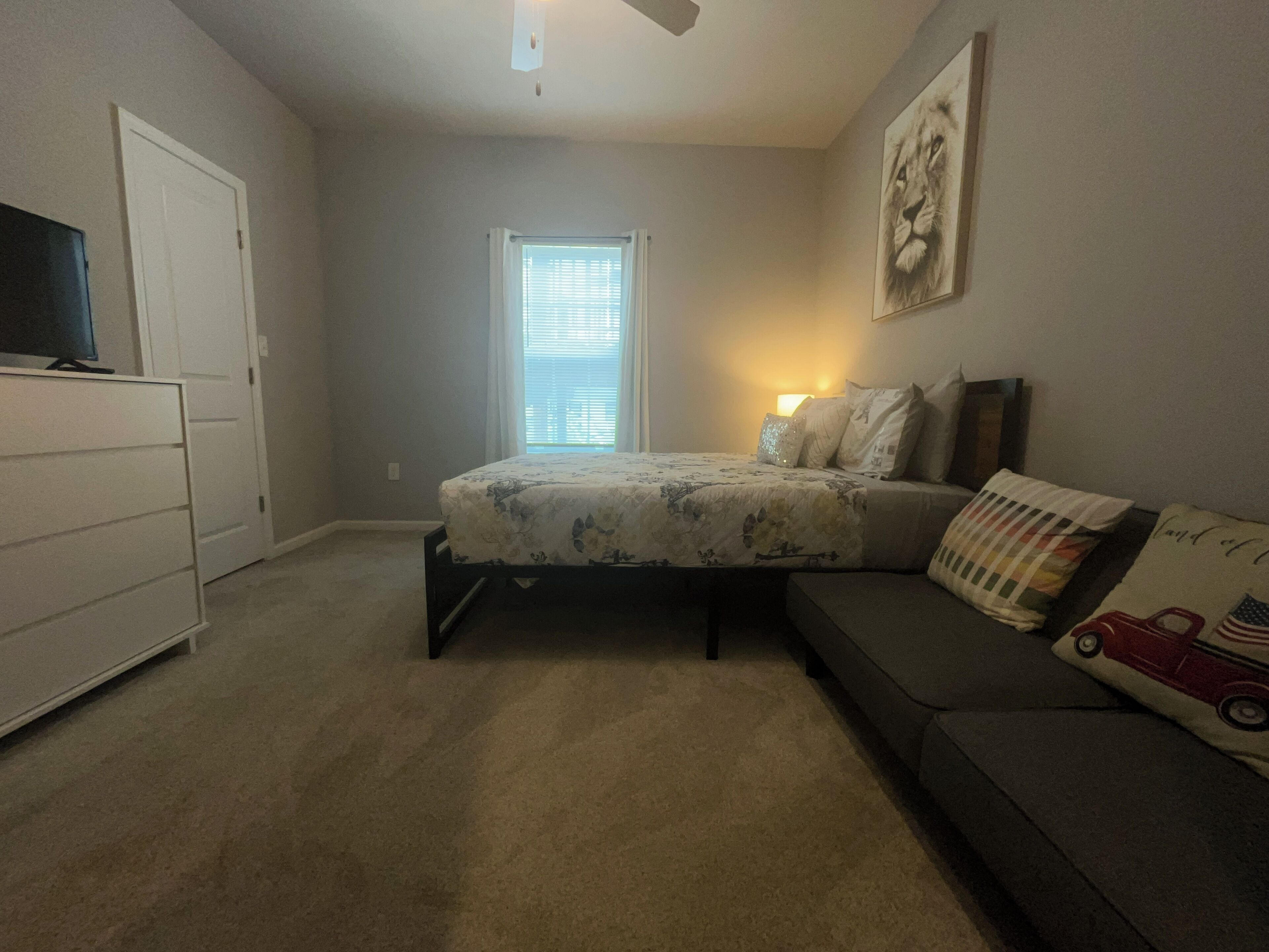 A bedroom with a bed, a dresser, a sofa, a window with blinds, and a ceiling fan.