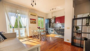 Une cuisine moderne avec des meubles de rangement rouges, un coin repas avec une table et des chaises en verre, et une grande fenêtre avec des rideaux.