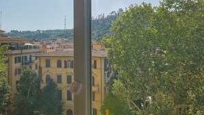 Une vue depuis une fenêtre, la lumière du soleil y filtre, donnant sur un parking où se trouvent plusieurs voitures et un immeuble à étages, doté de balcons.