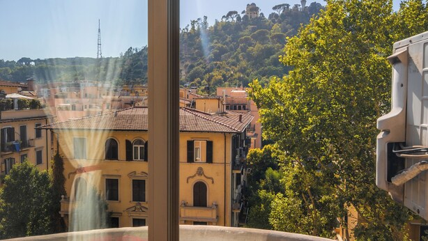 Une vue depuis une fenêtre donnant sur un paysage urbain, avec des bâtiments et des arbres.