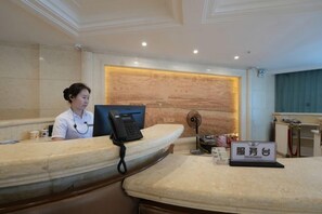 A reception desk with a receptionist, a computer, and a sign with Chinese characters. - Tumenjiang Business Hotel (Hunchun)