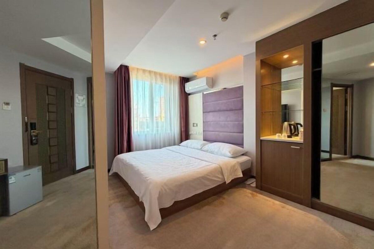 A hotel room with a bed, a wardrobe, a mirror, and a window with curtains.