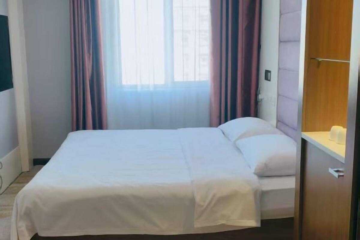 Ein Hotelzimmer mit Bett, Vorhängen, einem Fenster und einem Holzschrank.
