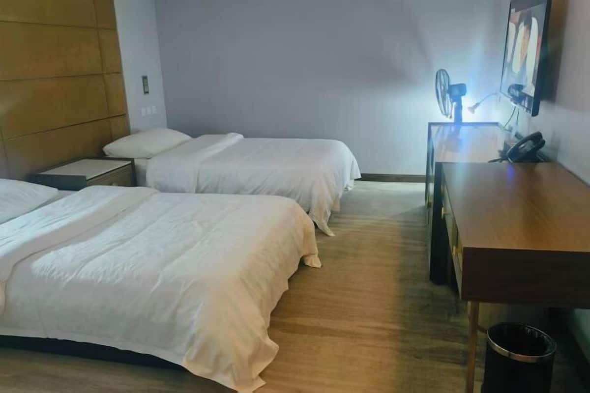 Ein Hotelzimmer mit zwei Betten, einem Holztisch, einem Stuhl, einem kleinen Tisch und einem an der Wand montierten Fernseher.