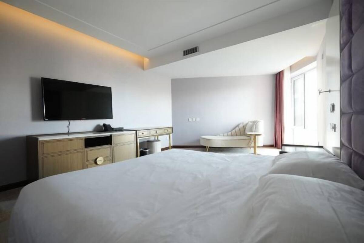 Ein modernes Hotelzimmer mit einem großen Bett, einem an der Wand befestigten Flachbildfernseher, einem Nachttisch und einem Sessel.