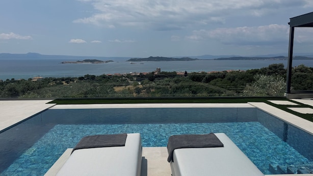 A swimming pool with two lounge chairs, a clear view of the sea and distant islands, and a modern architectural style.