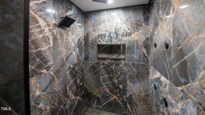 Une salle de bain moderne avec des murs en marbre, un espace douche et un luminaire au plafond.