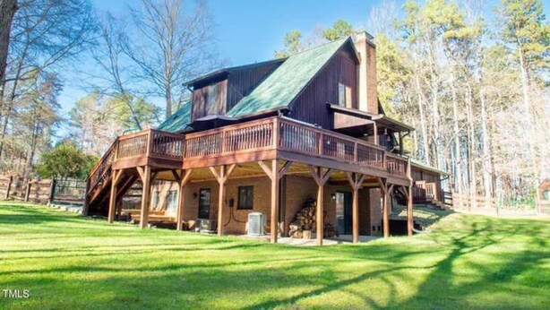 Une grande maison en bois avec un toit vert, plusieurs terrasses et une pelouse bien entretenue.