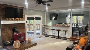 Un vaste salon doté d’une cheminée, d’un coin bar avec des tabourets et d’un espace repas offrant une vue sur l’extérieur.