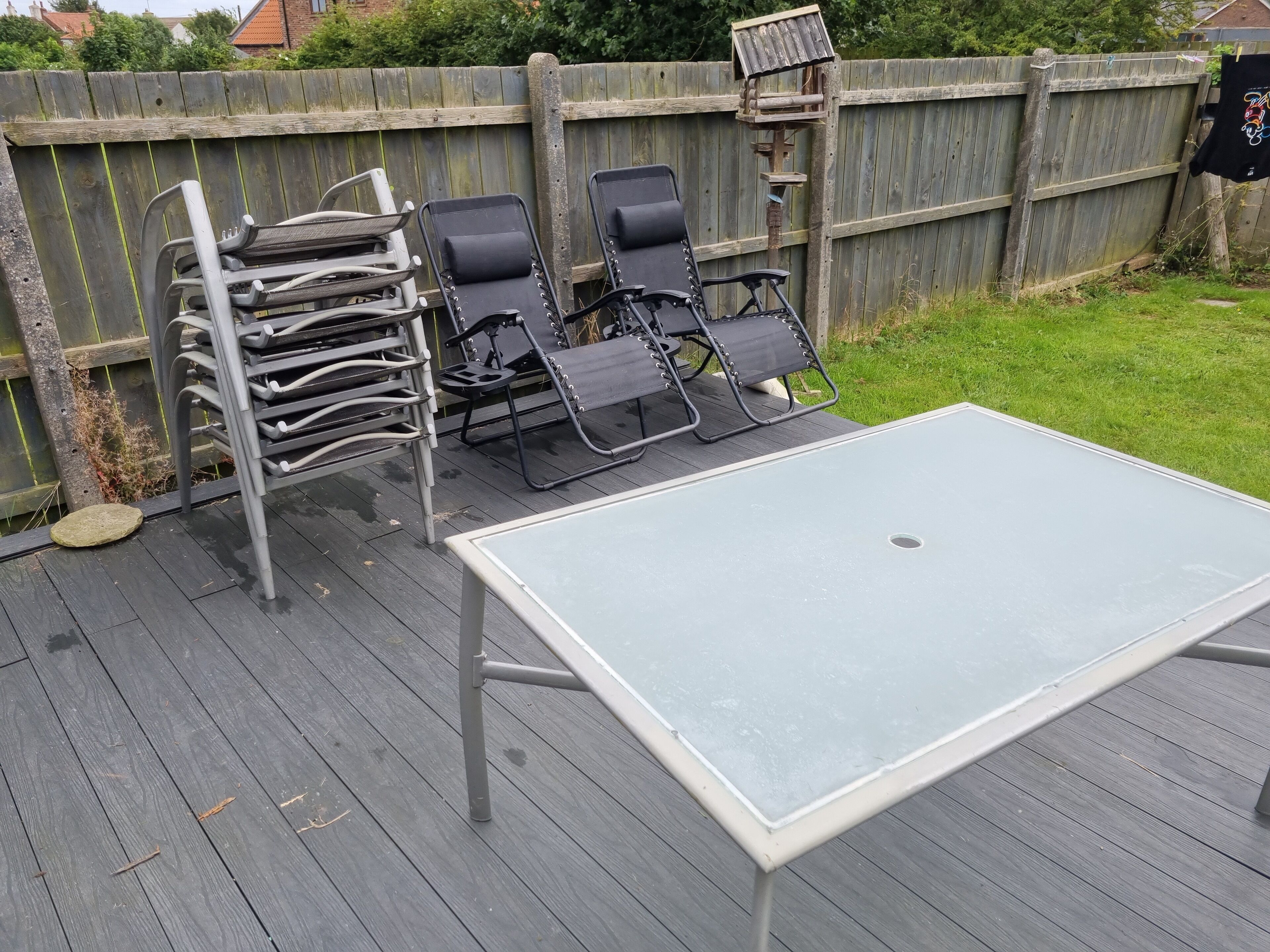 A deck with a table and two lounge chairs, a wooden fence in the background, and a bird feeder.