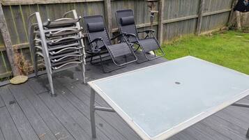 A deck with a table and two lounge chairs, a wooden fence in the background, and a bird feeder.