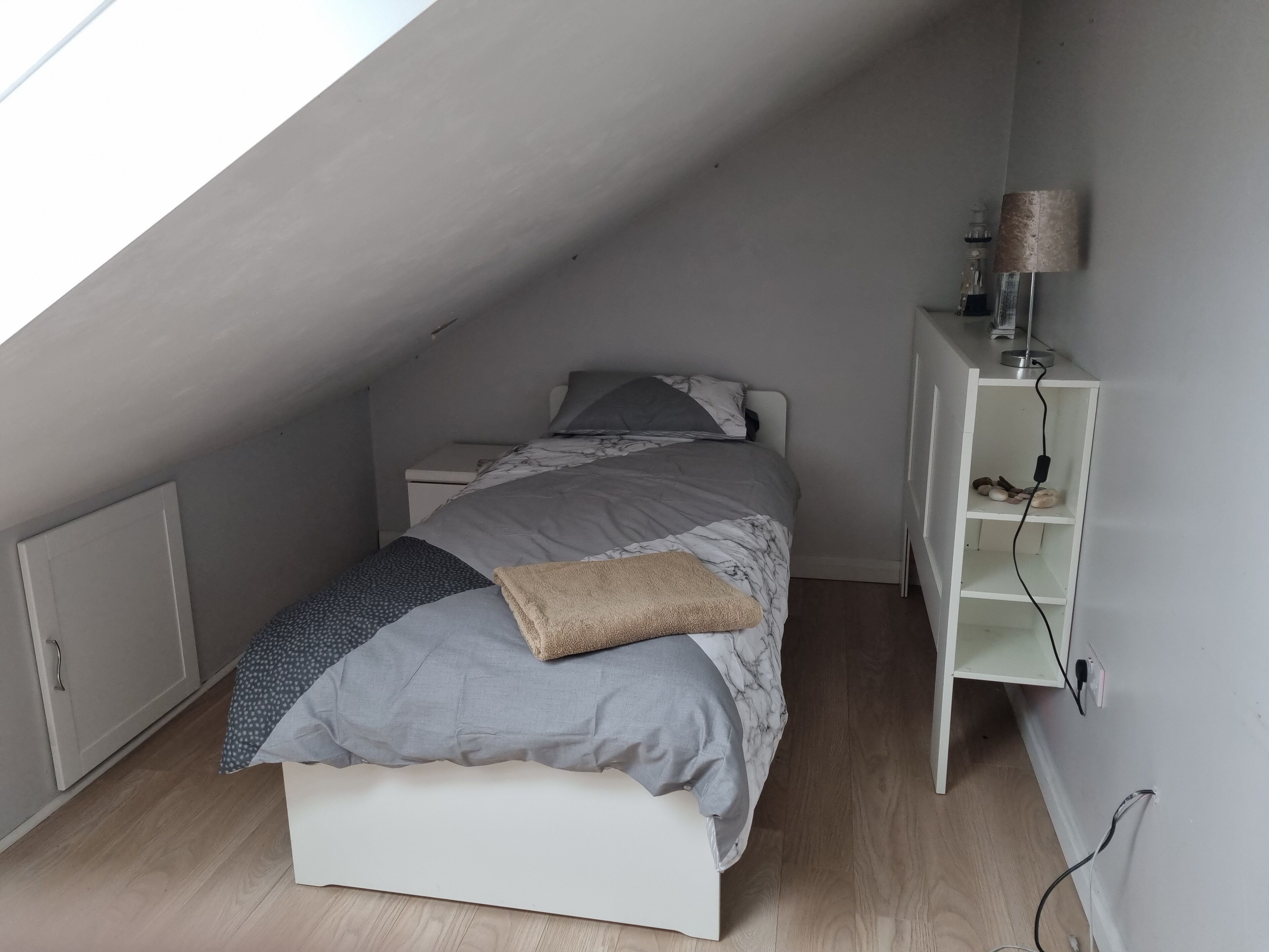 Un dormitorio con una cama, una mesita de noche, una lámpara y un armario blanco.