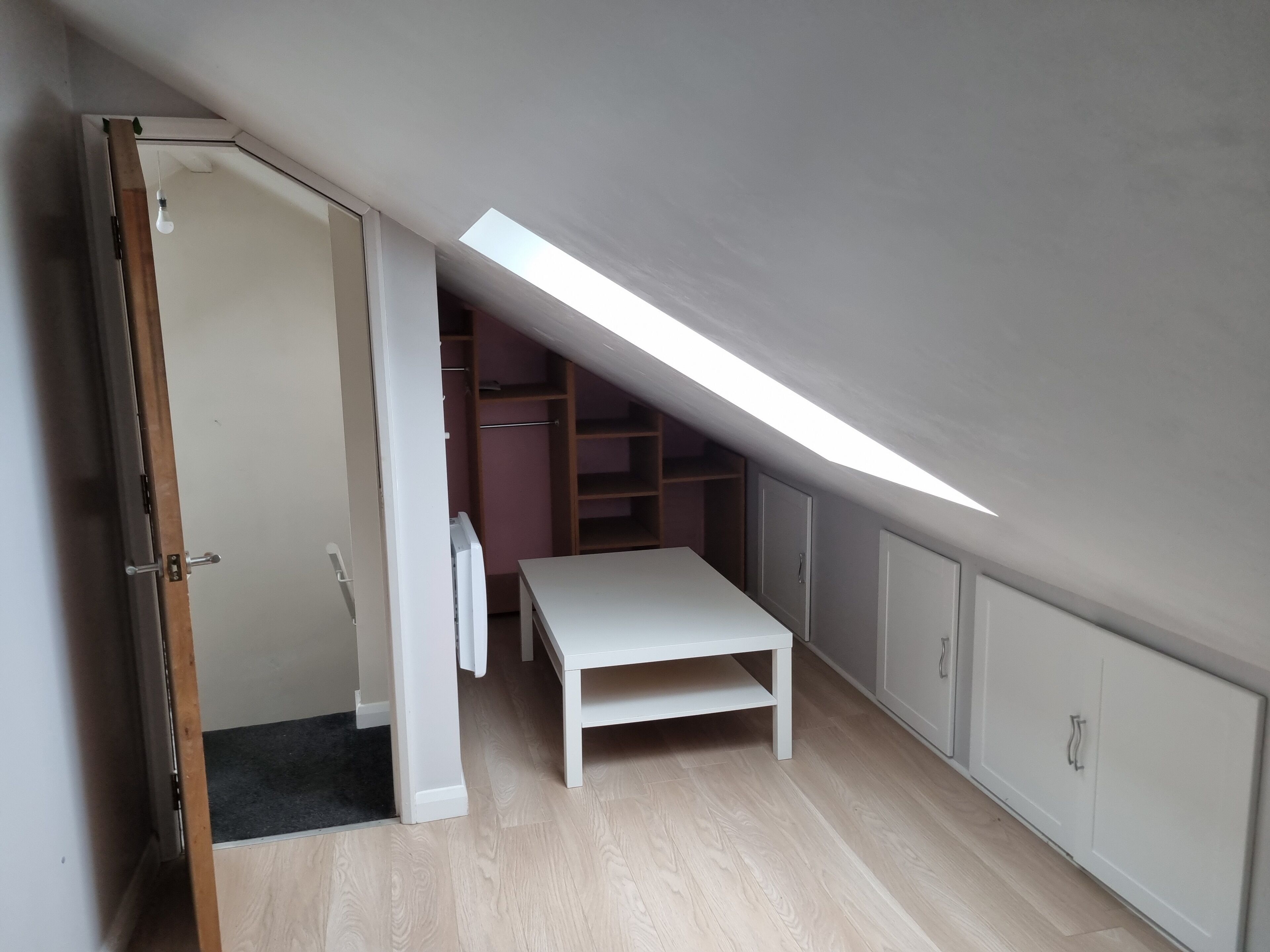 A room with a sloped ceiling, a white table, and built-in shelving.